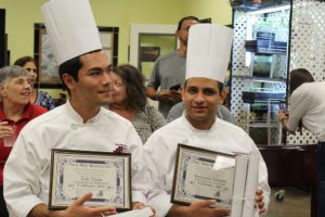 Two chefs are holding their certificates in a restaurant.